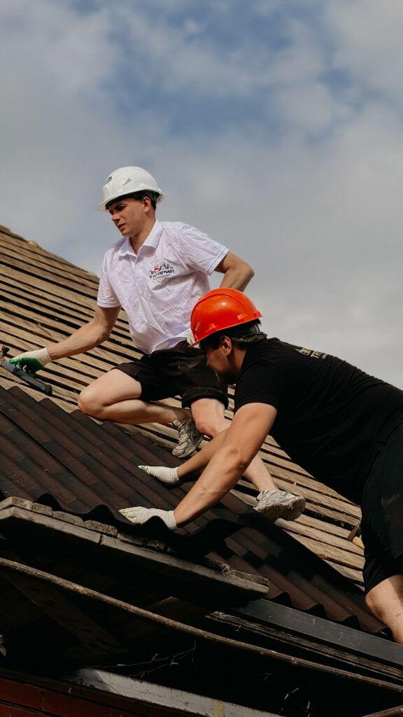 Two roofers in safety helmets working on a residential roof under clear skies
