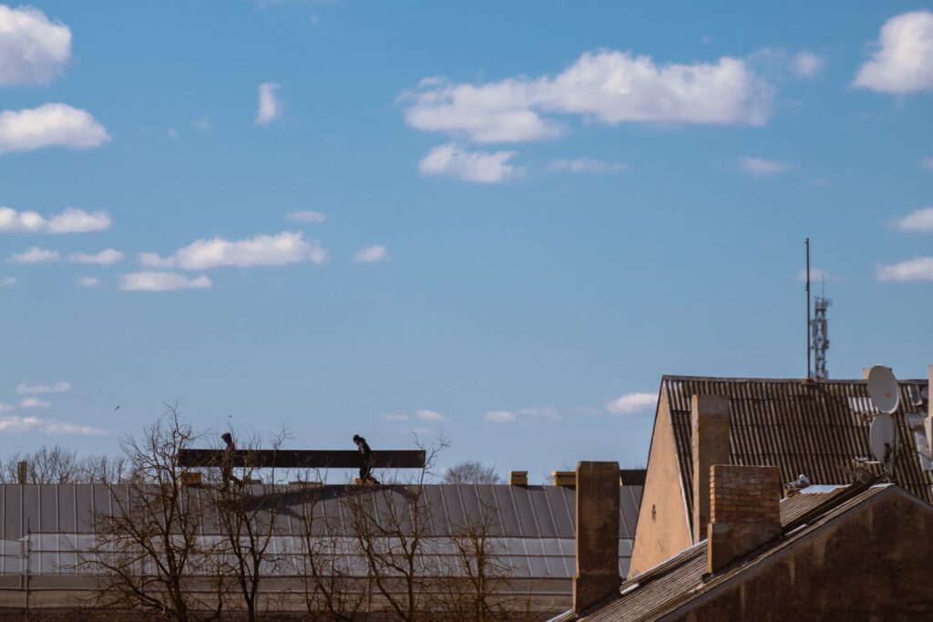 Silhouetted roofing crew working on a roof under a partly cloudy sky